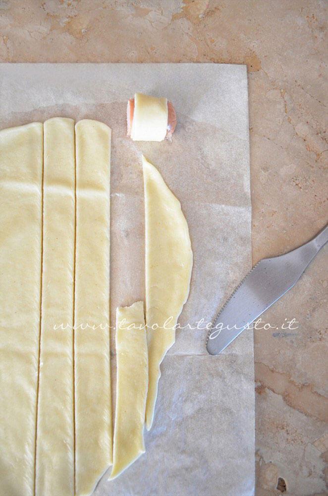 Avvolgere ogni pezzetto in una striscia di pasta brisee - Ricetta Rotolini di Wurstel in brisee Avvolgere ogni pezzetto in una striscia di pasta brisee - Ricetta Rotolini di Wurstel in brisee