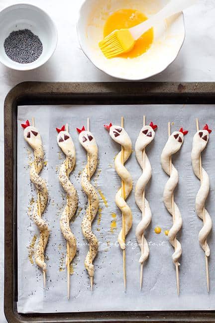 Pennellare i serpenti di pizza e spolverare con semi di papavero - Ricetta Serpenti di pizza per Halloween