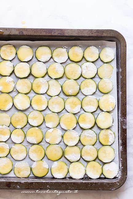Condire le patatine di zucchine con un filo d'olio e cuocere in forno - Ricetta Chips di zucchine