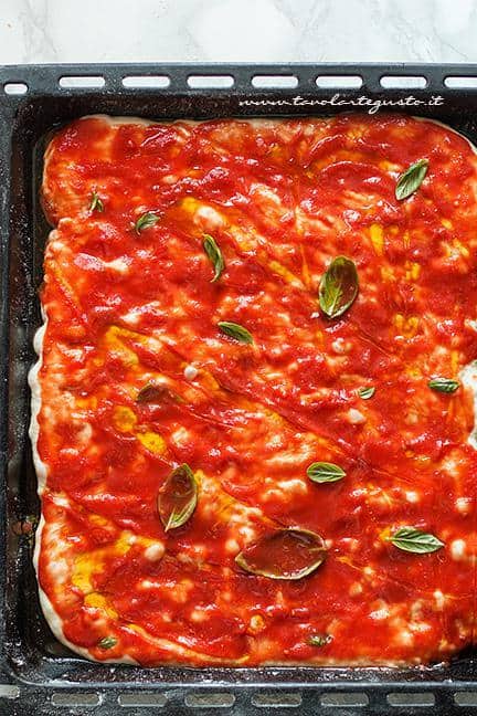 Condire la pizza con pomodori pelati, basilico e olio - Ricetta pizza in teglia